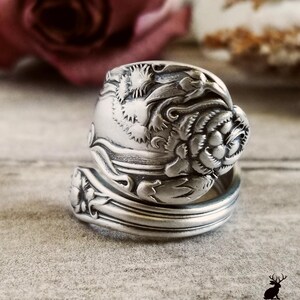 May include: A silver spoon ring with a floral design. The ring is made from a vintage spoon and features a rose with leaves.
