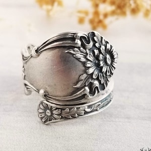 May include: A silver spoon ring with a floral design. The ring is made from a vintage spoon and features a delicate floral pattern.