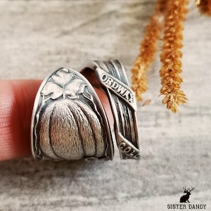 May include: Two silver rings, one with a detailed pumpkin design and the other with the words "ORDWAY" and "COLO" engraved on it.