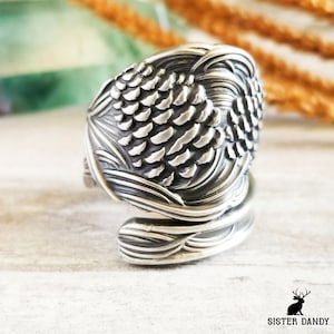 May include: A silver ring with a detailed design of a pine cone. The ring is made from a recycled spoon and is a unique piece of jewelry.