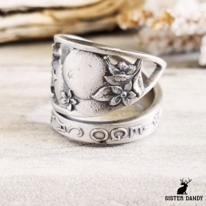 May include: A silver spoon ring with a floral design and the words "Sister Dandy" engraved on the band.