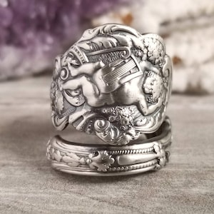 May include: Silver spoon ring featuring a cherub playing a lyre. The ring is made from a vintage spoon and is a unique piece of jewelry.