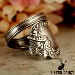 Puede incluir: Un anillo de plata hecho a mano a partir de una cuchara, con detalles ornamentados en el cuenco de la cuchara. El anillo tiene una banda curvada y un dise&ntilde;o decorativo en la cara, mostrando una est&eacute;tica vintage &uacute;nica.