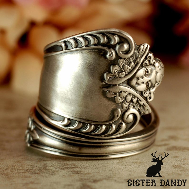 Puede incluir: Un anillo de plata hecho con una cuchara, con detalles ornamentados. El anillo presenta un dise&ntilde;o de querub&iacute;n esculpido y adornos decorativos. Una joya &uacute;nica.