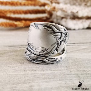 May include: A silver spoon ring with a floral design. The ring is made from a vintage spoon and is a unique piece of jewelry.