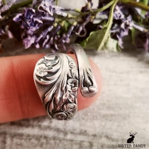May include: A silver spoon ring with a floral design. The ring is made from a vintage spoon and is a unique piece of jewelry.