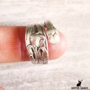 May include: Silver ring with a floral design. The ring is made from a repurposed spoon and features a delicate flower design.