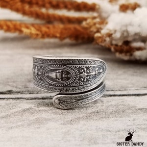 May include: A silver ring made from a vintage spoon with an ornate design. The ring is wrapped around the finger and has a detailed pattern of swirls and flowers.