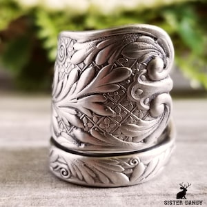 Könnte beinhalten: Nahaufnahme eines silbernen Rings mit aufwendigen Blumen- und Blattmustern. Der Ring hat ein detailliertes, geprägtes Design mit Vintage-Ästhetik. Der Ring ist wahrscheinlich ein Statement-Schmuckstück.