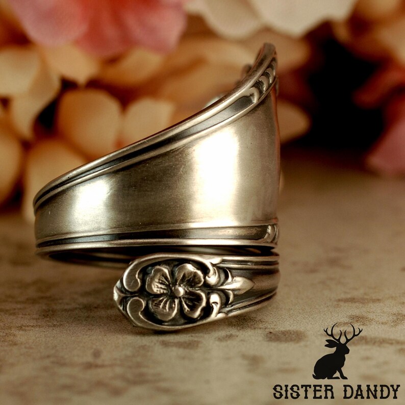 Puede incluir: Un anillo de plata hecho de una cuchara, con un dise&ntilde;o floral en el cuenco de la cuchara. El anillo est&aacute; envuelto, mostrando el mango y el cuenco de la cuchara. El anillo es de metal brillante, el fondo est&aacute; borroso.