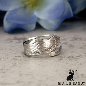 May include: A silver-toned ring with a textured, leaf-like design. The ring wraps around the finger with an open, adjustable design. The word "order" is engraved on the band. The ring is set against a neutral background.