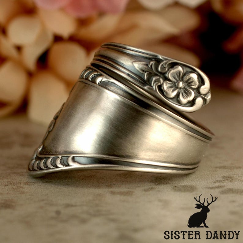 Puede incluir: Anillo de plata hecho a mano a partir de una cuchara, con un dise&ntilde;o floral en el cuenco de la cuchara. El anillo tiene un acabado de metal cepillado y un dise&ntilde;o art&iacute;stico &uacute;nico. Una pieza de joyer&iacute;a llamativa.