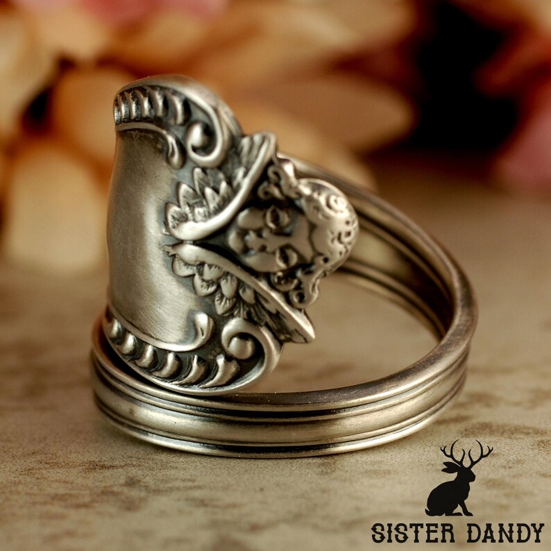 Puede incluir: Un anillo de plata hecho a mano con detalles ornamentados. El anillo presenta un dise&ntilde;o decorativo en la cara y una banda hecha del mango de la cuchara. Una pieza de joyer&iacute;a &uacute;nica.