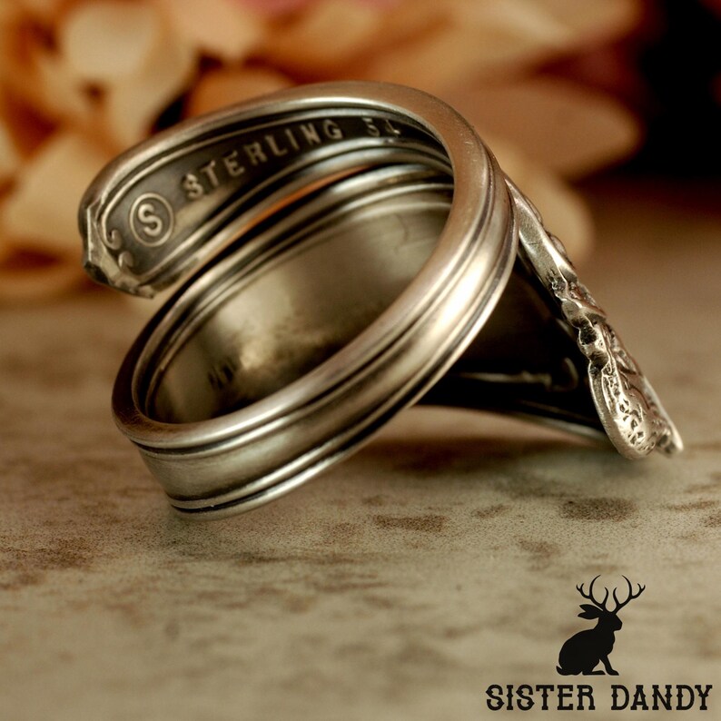 Puede incluir: Un anillo de plata hecho a mano a partir de una cuchara, con la palabra "STERLING" visible. El anillo tiene un dise&ntilde;o curvado, con el mango de la cuchara formando la banda. Una pieza de joyer&iacute;a &uacute;nica.