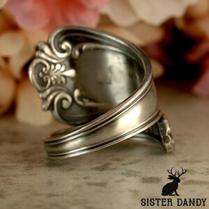 Puede incluir: Un anillo de plata con forma de cuchara, con intrincados detalles florales y de volutas. El anillo est&aacute; hecho de una cuchara reutilizada, con la cuchara formando la cara del anillo. La banda se envuelve, creando un accesorio &uacute;nico de inspiraci&oacute;n vintage.