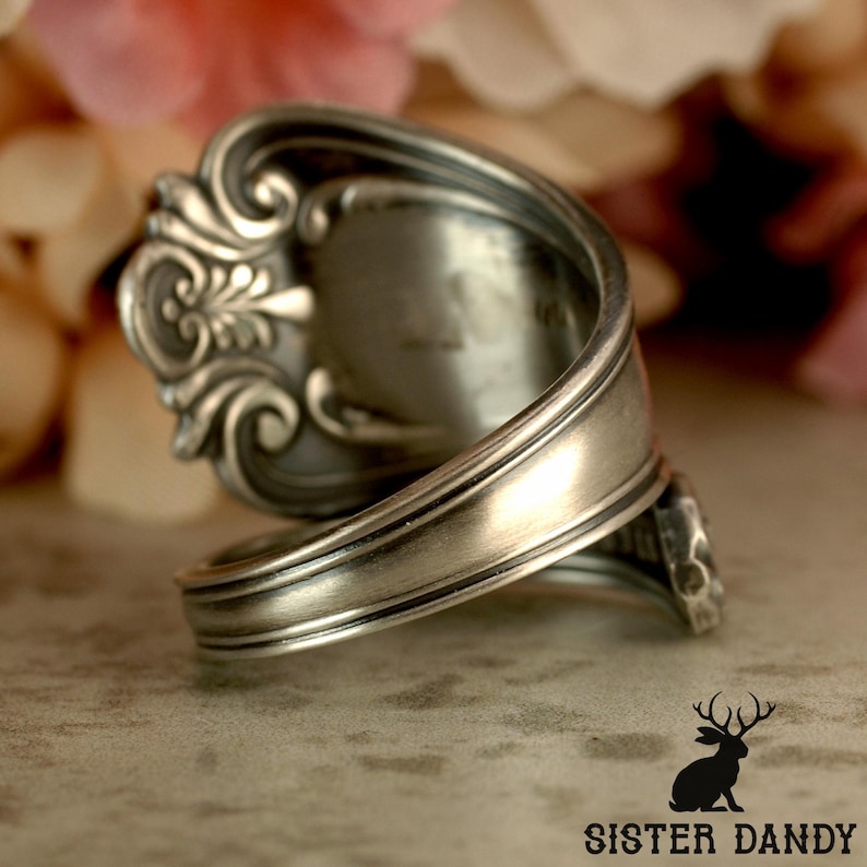 Puede incluir: Un anillo de plata con forma de cuchara, con intrincados detalles florales y de volutas. El anillo est&aacute; hecho de una cuchara reutilizada, con la cuchara formando la cara del anillo. La banda se envuelve, creando un accesorio &uacute;nico de inspiraci&oacute;n vintage.