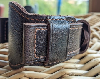 May include: A dark brown leather watch strap with a stitched edge. The strap is designed to be adjustable and has a buckle closure.