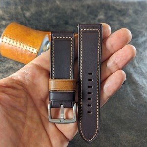 Può includere: Due cinturini per orologio in pelle marrone con cuciture a contrasto beige. Un cinturino ha una fibbia argentata.