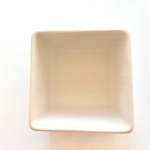 May include: A white ceramic square dish with a smooth, slightly textured surface. The dish is empty and ready to be used for serving or decorating.