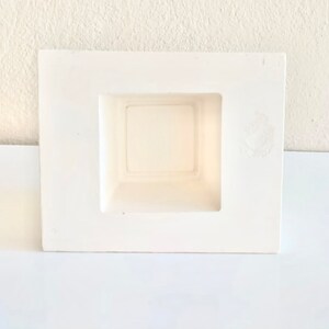 May include: White ceramic planter with a square opening. The planter is designed to be mounted on a wall.