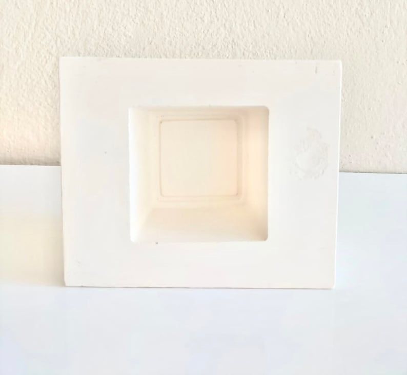 May include: White ceramic planter with a square opening. The planter is designed to be mounted on a wall.