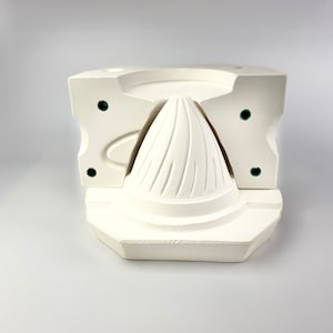 Puede incluir: Un molde de cerámica blanca para hacer un objeto con forma de cono. El molde está en tres piezas y tiene una superficie texturizada.