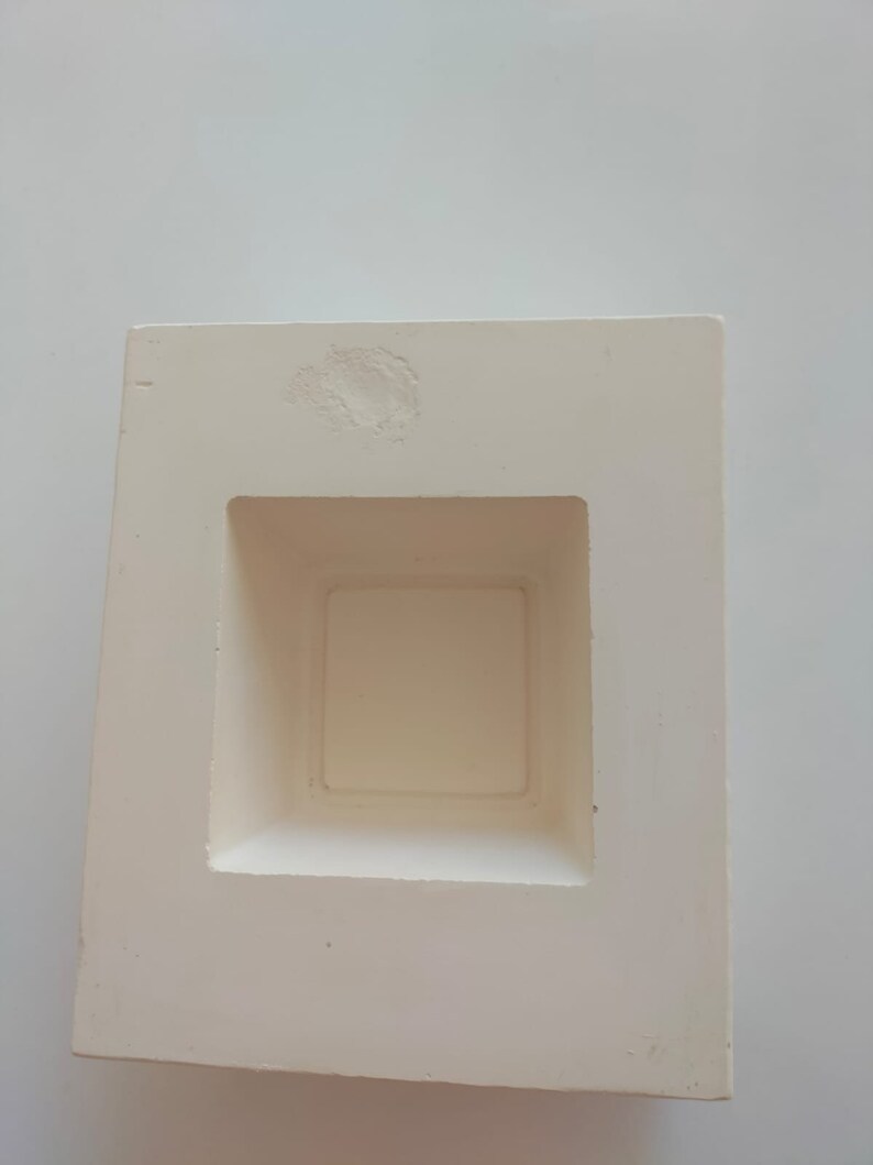 May include: White ceramic mold with a square opening in the center. The mold is designed for creating a square-shaped object.