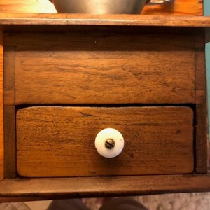 Op de afbeelding: Een houten doos met een lade en een witte knop. De doos is gemaakt van donker hout en heeft een eenvoudig ontwerp.