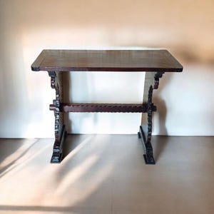 Puede incluir: Una mesa de madera marrón oscuro con un diseño tallado en las patas. La mesa tiene una tapa rectangular y un estilo rústico simple.