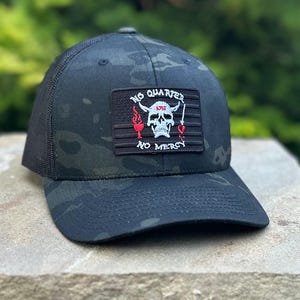 Puede incluir: Gorra de camionero de camuflaje negro y verde con un parche negro y rojo que dice "NO QUARTER NO MERCY" y presenta una calavera con cuernos y un corazón rojo.