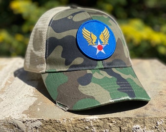 Może przedstawiać: Czapka trucker w kamuflażu z niebiesko-złotą naszywką przedstawiającą gwiazdę i skrzydła. Naszywka zawiera napis "USAF".