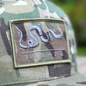 May include: A camouflage baseball cap with a patch featuring a stylised snake design and the text "JOIN OR DIE".