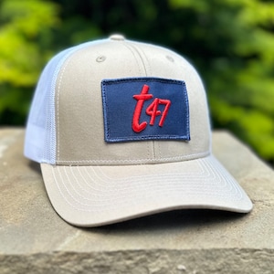 May include: A beige and white trucker hat with a navy blue and red patch that says "T47" on it.