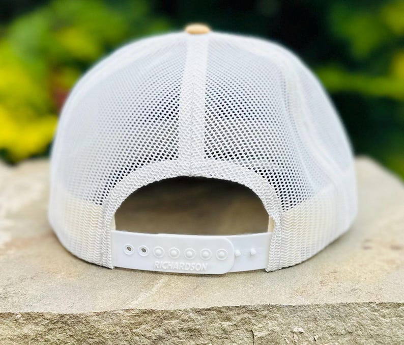 Puede incluir: Gorra de camionero de malla blanca con visera de color canela y una correa ajustable blanca con la palabra "Richardson" impresa.