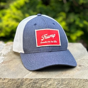 May include: A blue and white trucker cap with a red rectangular patch. The patch displays the name "Trump" in white script and the phrase "Smoother the 2nd Time". The cap has a mesh back.