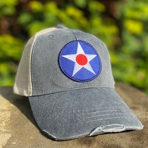 May include: A blue and white trucker hat with a distressed look. The hat has a round patch with a white star and a red center. The patch is on the front of the hat.