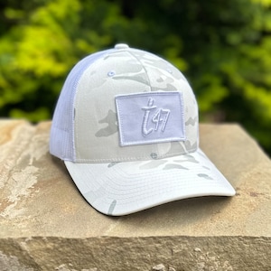 May include: White camouflage trucker hat with a white patch that says "T47" in a white script font.