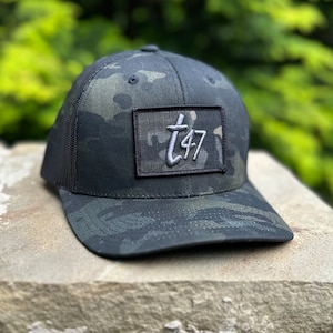 May include: Black and green camouflage trucker hat with a black patch that says "T47" in white lettering.