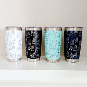 Peut inclure: Quatre gobelets YETI en acier inoxydable avec un motif de gnome. Les gobelets sont en blanc, noir, bleu clair et bleu marine.