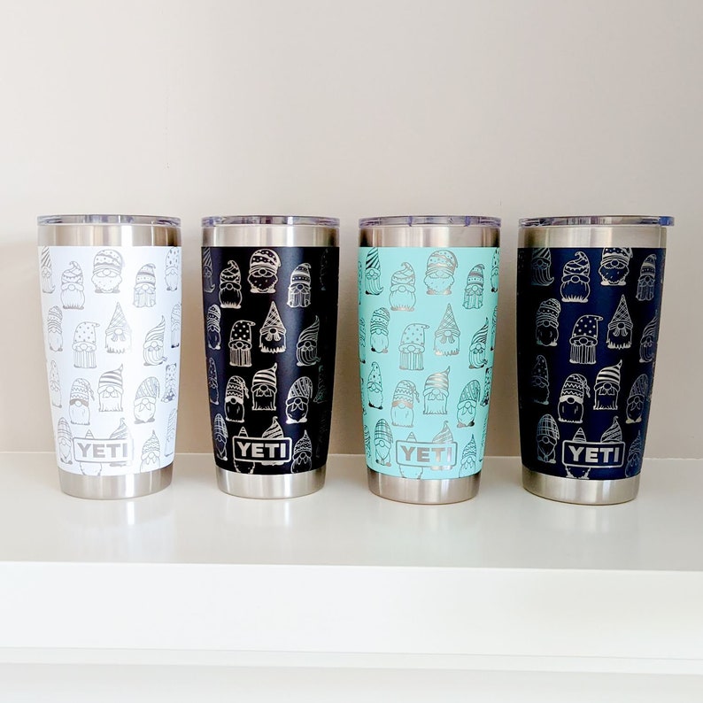 Peut inclure: Quatre gobelets YETI en acier inoxydable avec un motif de gnome. Les gobelets sont en blanc, noir, bleu clair et bleu marine.