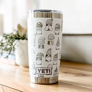 Peut inclure: Un gobelet Yeti blanc avec un couvercle et un fond en acier inoxydable. Le gobelet est recouvert d'un motif de gnomes noirs et blancs. Le mot "YETI" est imprim&eacute; en brun sur le devant du gobelet.