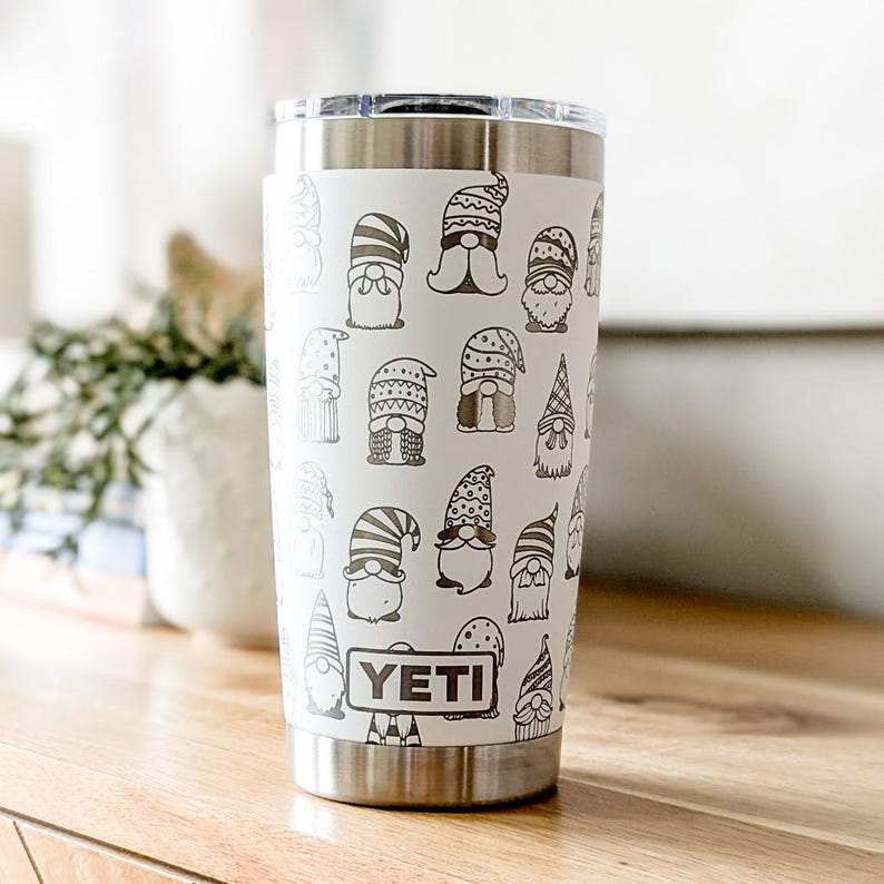 Peut inclure: Un gobelet Yeti blanc avec un couvercle et un fond en acier inoxydable. Le gobelet est recouvert d'un motif de gnomes noirs et blancs. Le mot "YETI" est imprim&eacute; en brun sur le devant du gobelet.
