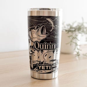 Laser-engraved stainless steel Yeti tumbler featuring a camping and fishing design, including an outdoor pine forest landscape and a person fishing from a boat on a lake.