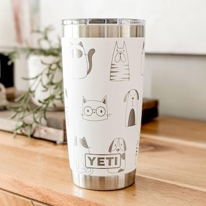 May include: White stainless steel YETI tumbler with a black and white pattern of cats and dogs. The tumbler has a lid and a black YETI logo.
