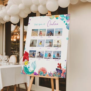 Puede incluir: Un tablero de exhibici&oacute;n de fotos personalizado con un tema de sirenas. El tablero muestra doce fotos, cada una representando un mes, con el texto "First year of Ondina". Ilustraciones coloridas de sirenas y del oc&eacute;ano adornan la parte inferior.