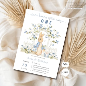 以下が含まれることがあります： 青いジャケットを着たウサギの水彩イラストが描かれた5x7インチの招待状。花と白い柵に囲まれています。「some bunny is turning ONE」というテキストとイベントの詳細が含まれています。