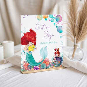 May include: A decorative sign featuring a mermaid with red hair and a teal tail, holding a yellow fish. The sign has the words "Custom Sign" and "Optional text here" with colorful bubbles and coral reef illustrations.
