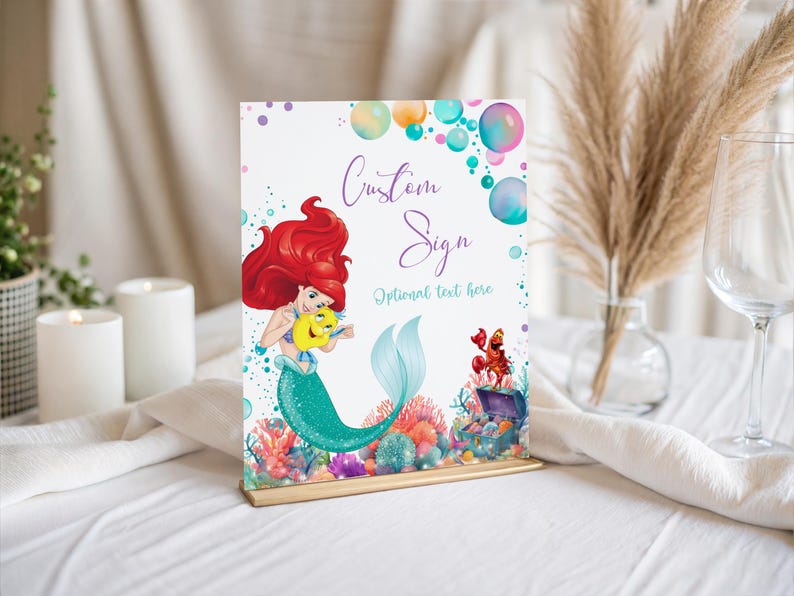 May include: A decorative sign featuring a mermaid with red hair and a teal tail, holding a yellow fish. The sign has the words "Custom Sign" and "Optional text here" with colorful bubbles and coral reef illustrations.