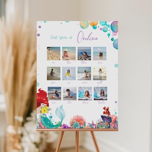 Puede incluir: Un tablero de exhibici&oacute;n de fotos personalizado con tem&aacute;tica de sirenas con el texto "First Year of Ondina". El tablero presenta doce fotos peque&ntilde;as, burbujas coloridas e ilustraciones de sirenas. El tablero se exhibe en un caballete de cobre.