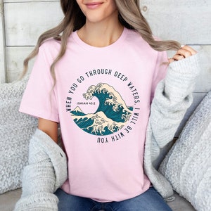 May include: Pink t-shirt with a blue and white wave graphic and the text "When you go through deep waters, I will be with you. Isaiah 43:2"